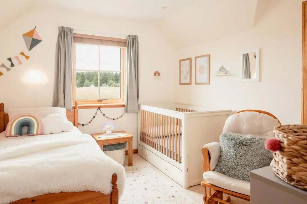 a childs bedroom with a crib and a chair at Balnagowan Cottage in Nethy Bridge