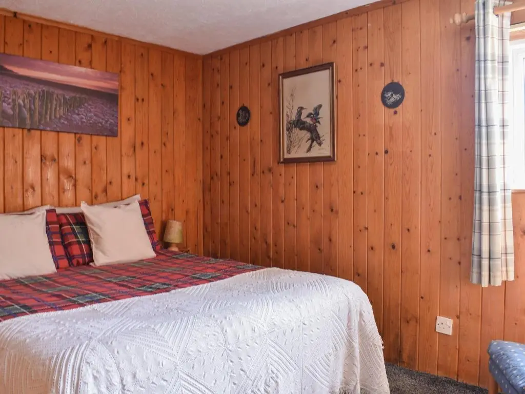 a bedroom with wooden walls and a bed with white sheets at The Bothy - Ukc5785 in Nethy Bridge