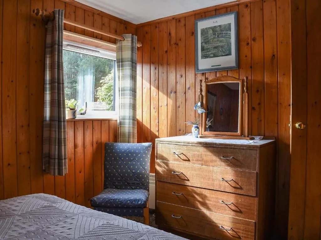 a bedroom with a dresser and a chair and a mirror at The Bothy - Ukc5785 in Nethy Bridge