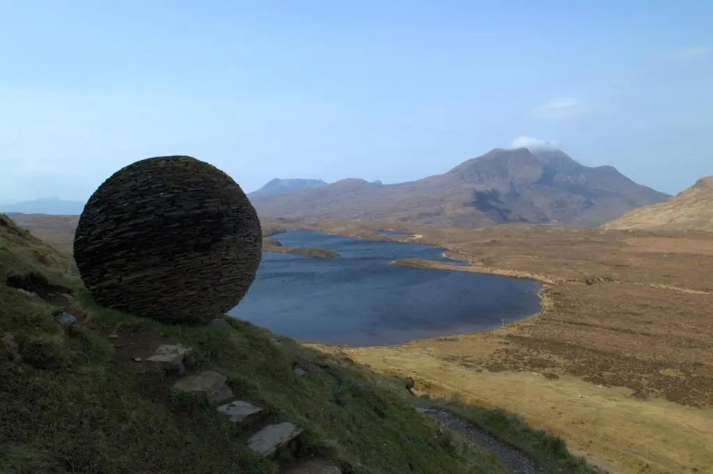 a large rock on a hill next to a body of water at Rosemount Cottage TWO - Highland Cottage in Garve