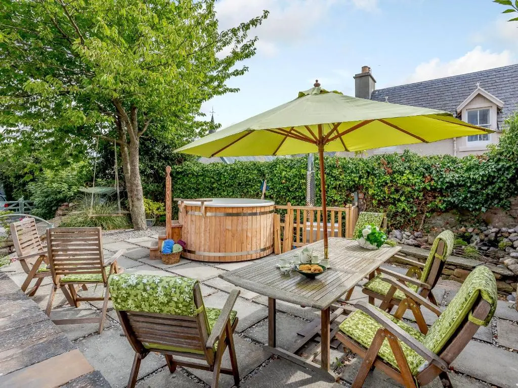 a wooden table with chairs and an umbrella at Caldon Cottage in Cromarty
