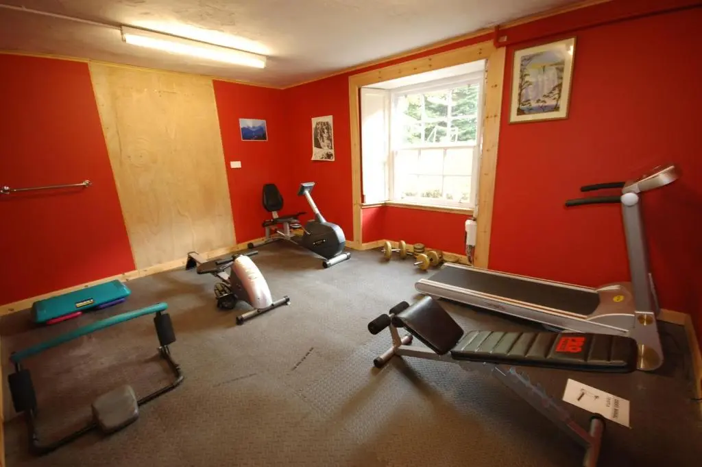a gym with cardio equipment in a room with red walls at The Old Manse, Fochabers in Fochabers