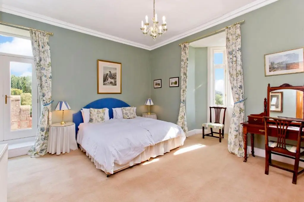 a bedroom with a bed and a desk and windows at Dalnaglar Castle in Blairgowrie