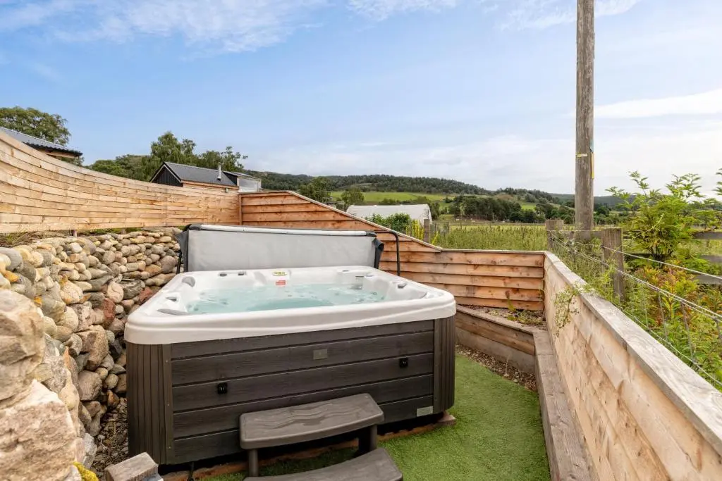 a hot tub in a garden with a stone wall at Alba - Charming boutique forest view cabin with hot tub in Ballater in Ballater