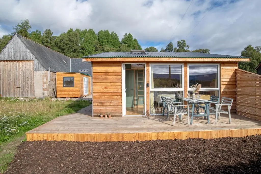 a small cabin with a table and chairs on a deck at Alba - Charming boutique forest view cabin with hot tub in Ballater in Ballater