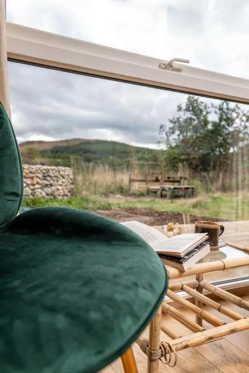 a green chair sitting in front of a window at Alba - Charming boutique forest view cabin with hot tub in Ballater in Ballater