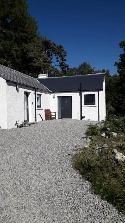 a white house with a black roof and a gravel driveway at Torgoyle Cottage in Inverness