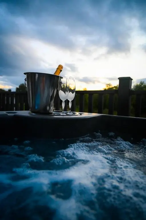 a hot tub with a bucket and a wine glass at Newmore Highland Pods with Hot Tubs on NC500 in Invergordon