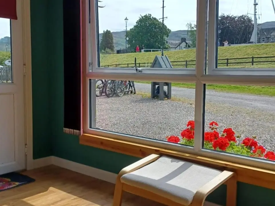 a window with a view of a park with red flowers at Erraid Lodge in Fort Augustus