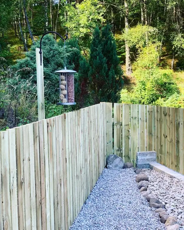 a wooden fence with a bird feeder hanging over it at Loch Ness Woodland Pods in Drumnadrochit