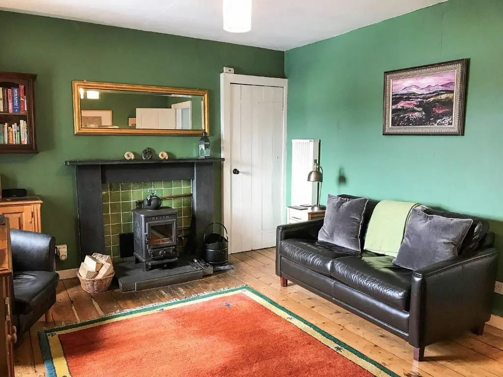 a living room with a black leather couch and a fireplace at Tigh Beag in Newtonmore