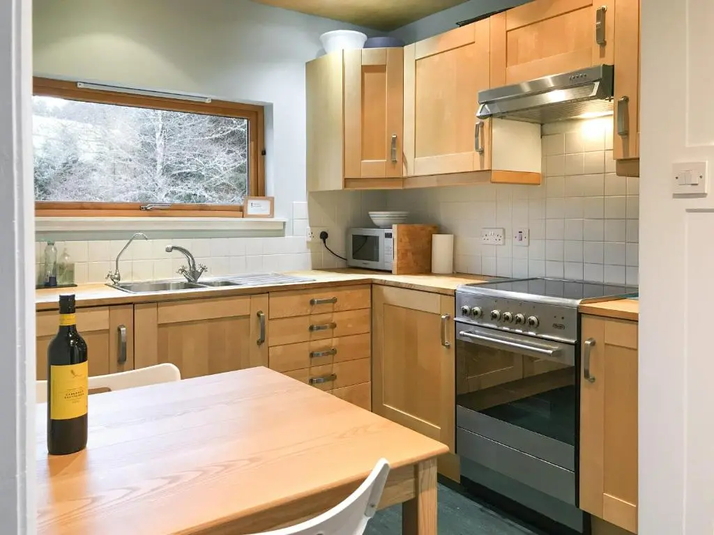 a kitchen with wooden cabinets and a table with a bottle of wine at Tigh Beag in Newtonmore