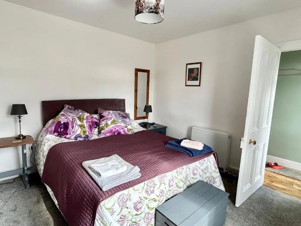 a bedroom with a bed with a purple bedspread at Lottie\u2019s Cottage, Rhynie, Aberdeenshire in Rhynie