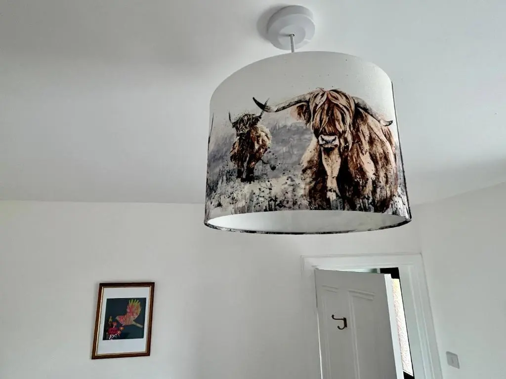 a light hanging from a ceiling with a painting of a cow at Lottie\u2019s Cottage, Rhynie, Aberdeenshire in Rhynie