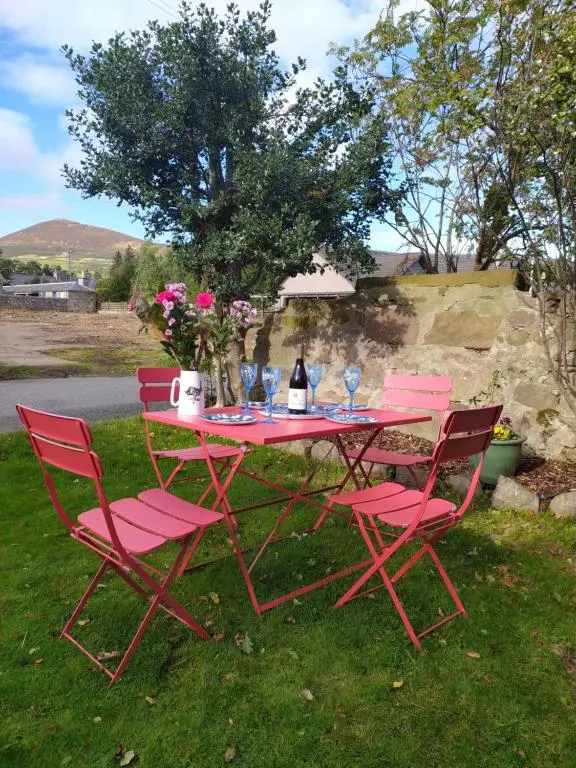 a red picnic table with pink chairs and a bottle of wine at Lottie\u2019s Cottage, Rhynie, Aberdeenshire in Rhynie