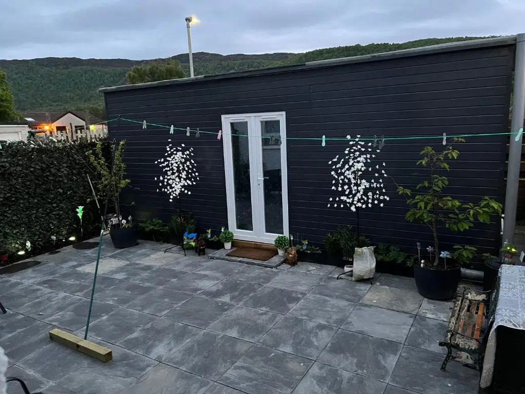 a black house with a patio with potted plants at Craigellachie Cabin in Aviemore