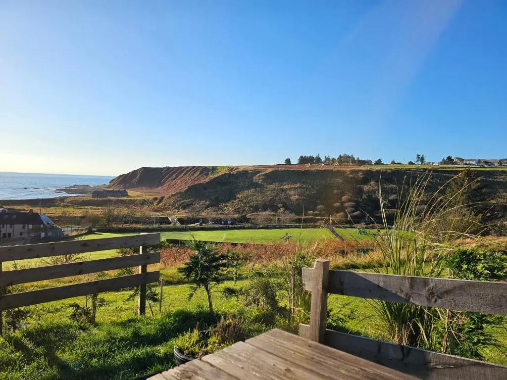 a bench overlooking the ocean with a hill in the background at Dunbeath Coastal Retreat in Dunbeath