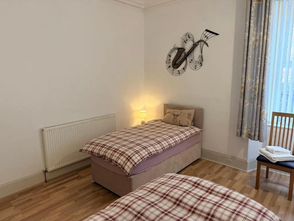 a small bedroom with a bed and a guitar on the wall at Spacious 2 Bedroom Flat in heart of Ballater in Ballater