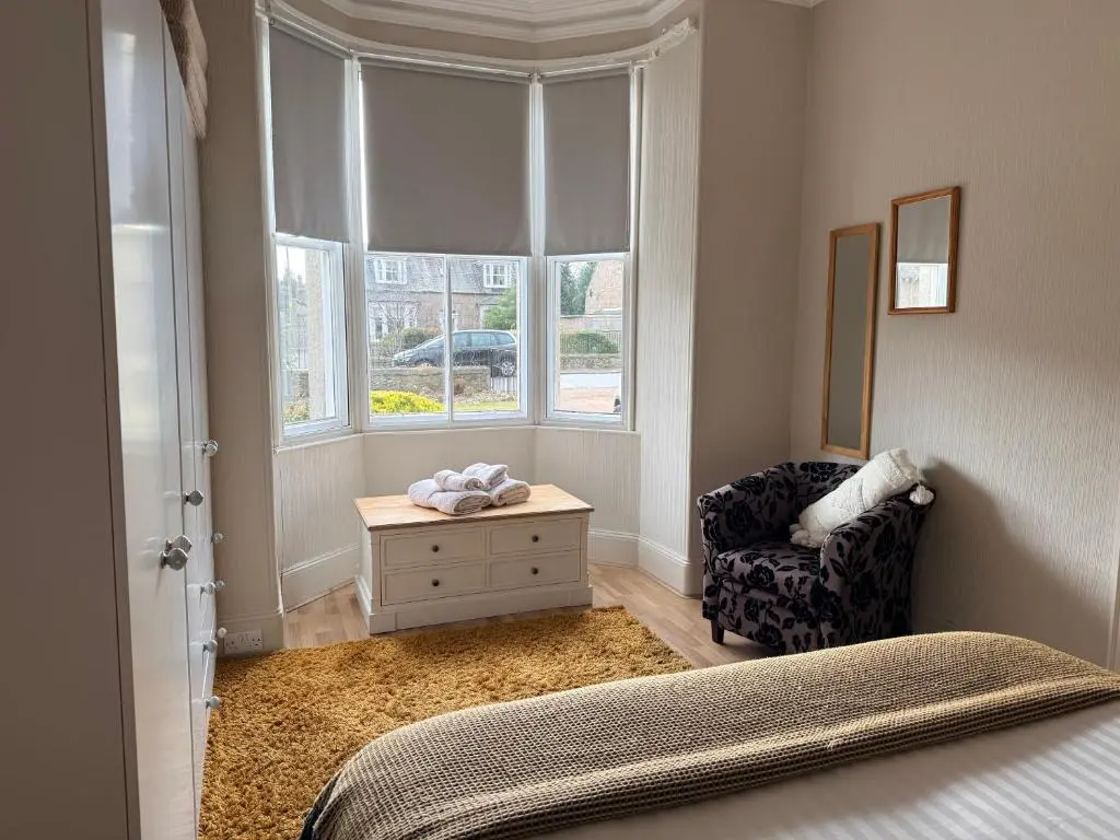 a bedroom with a bed and a chair and a window at Spacious 2 Bedroom Flat in heart of Ballater in Ballater