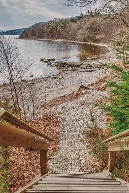 a wooden bench sitting next to a body of water at Loch Ness Mansion in Invermoriston