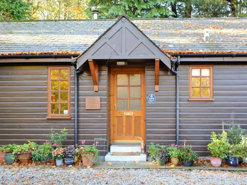 a gray house with a brown door and some plants at Toll Bridge Lodge in Banchory