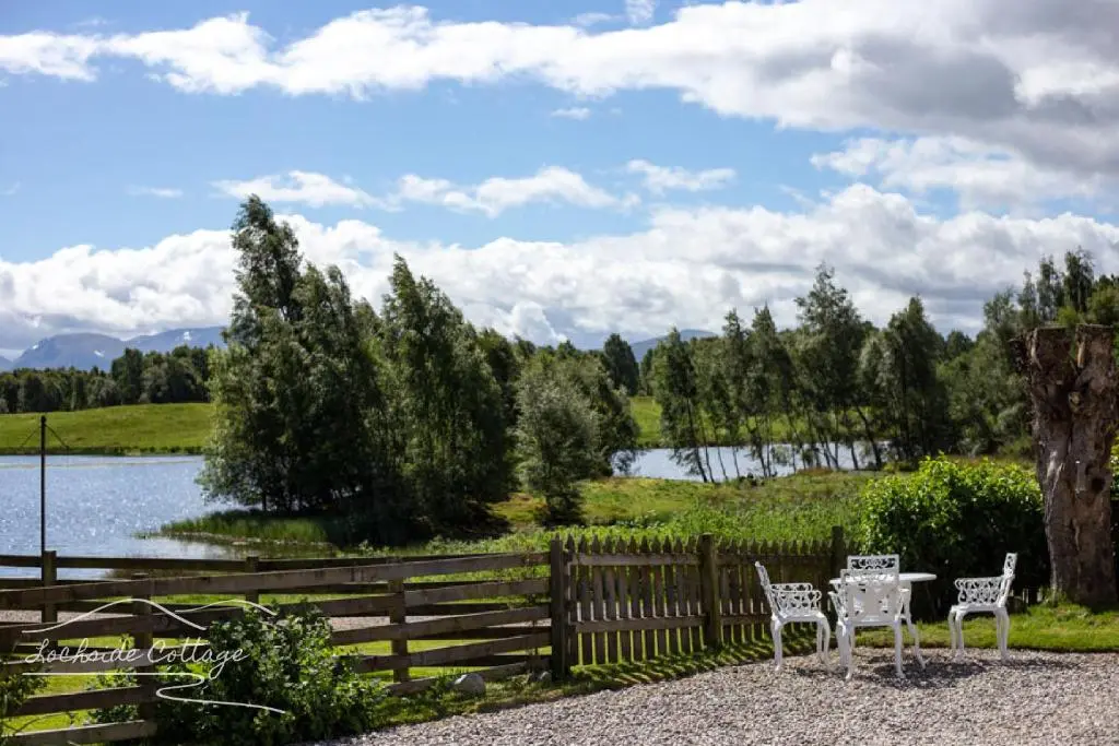 two chairs and a table next to a fence and a lake at Lochside Cottage - near Aviemore in Aviemore