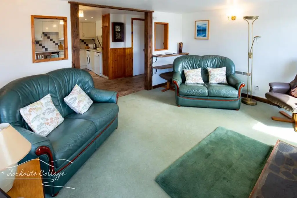 a living room with two leather couches and a kitchen at Lochside Cottage - near Aviemore in Aviemore