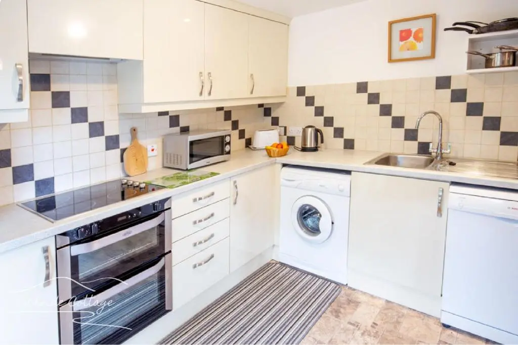 a kitchen with white cabinets and a washer and dryer at Lochside Cottage - near Aviemore in Aviemore