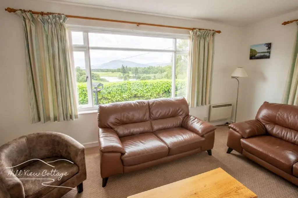 a living room with a leather couch and a chair at Hill View Cottage - near Aviemore in Aviemore
