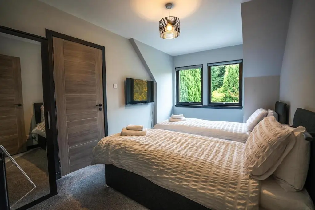a bedroom with two beds and two windows at FAMILY FRIENDLY, HOT TUB, Fire Pit, Spacious & Modern in Fochabers