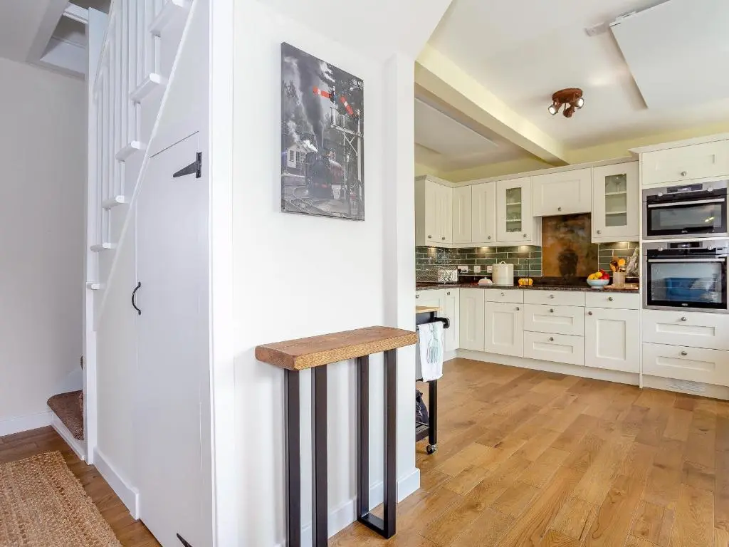 a kitchen with white cabinets and a wooden floor at Woodford - Cottage in Boat of Garten
