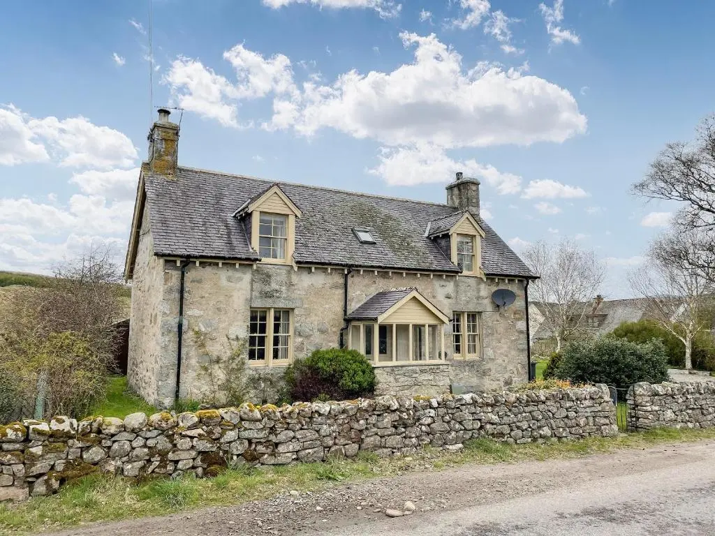 an old stone house with a stone wall at Milton Cottages in Invercassley