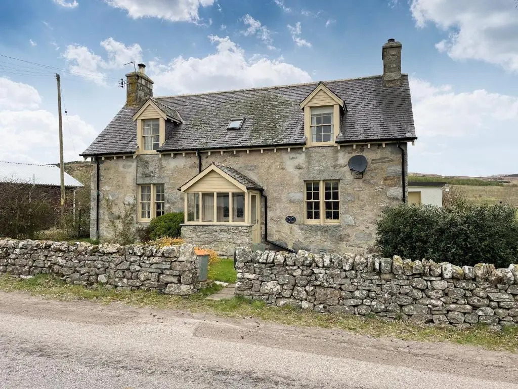 an old stone house with a stone wall at Milton Cottages in Invercassley