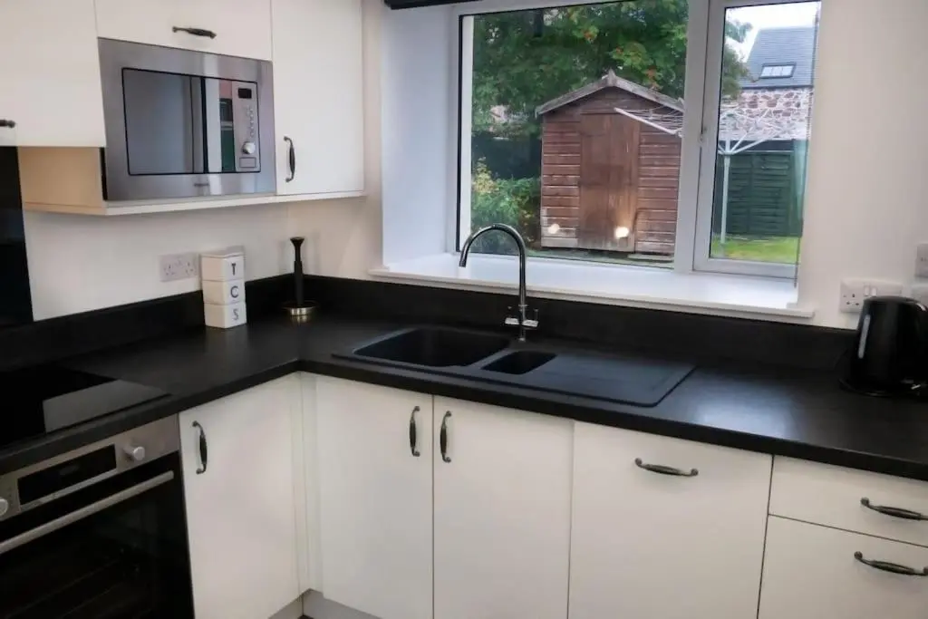 a kitchen with white cabinets and a sink and two windows at Central 2 bedroom luxury home close to River Ness in Inverness