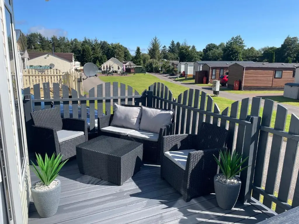 a patio with wicker chairs and a bench and a fence at Freedom Lodge-Aviemore with FREE Starlink Superfast broadband 150mbps - All bedding and towels included - Pet Free in Aviemore