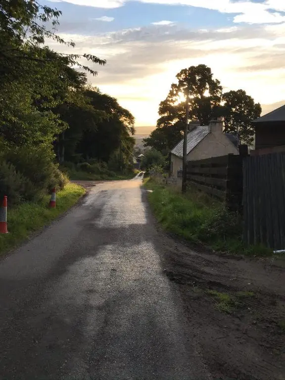 an empty road with the sun setting on the horizon at Woodside Cabin in Inverness