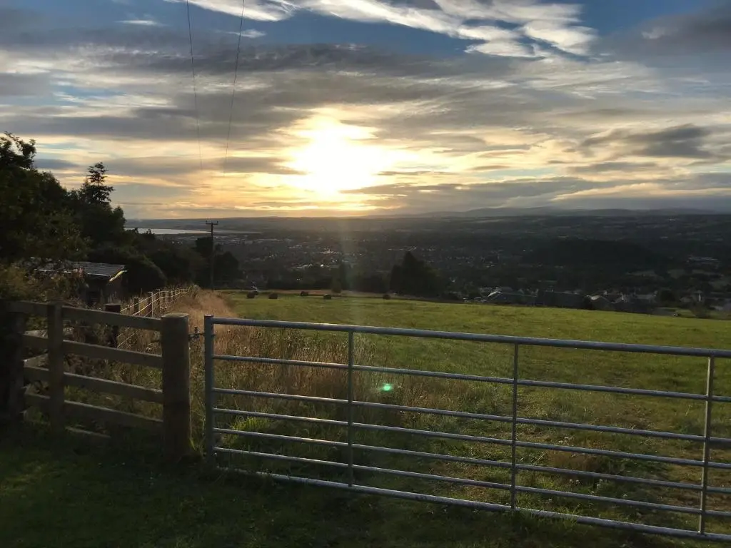 a fence on a hill with the sunset in the background at Woodside Cabin in Inverness