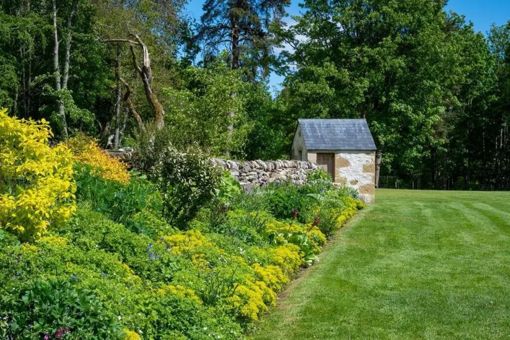 a garden with a stone wall and a small building at Assynt House - Exclusive Use Holiday House in Dingwall