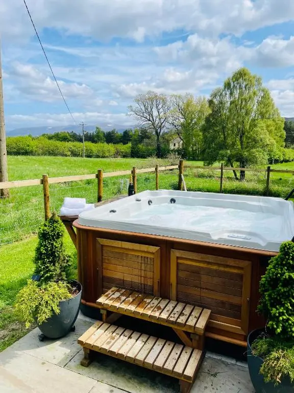 a jacuzzi tub in a yard with a field at Stag's Hide in Aviemore