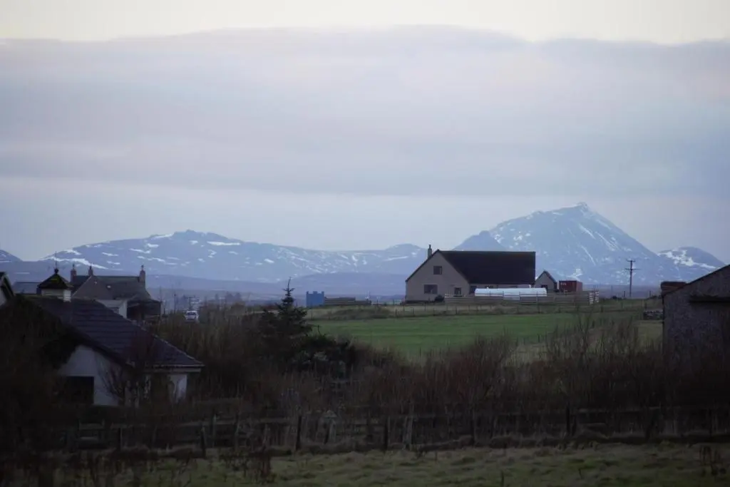 a group of houses in a field with mountains in the background at The Windy Roost in Occumster