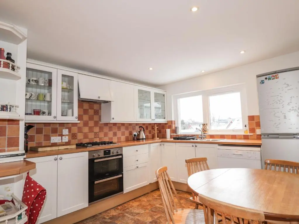 a kitchen with white cabinets and a table and a dining room at The Larches in Kingussie