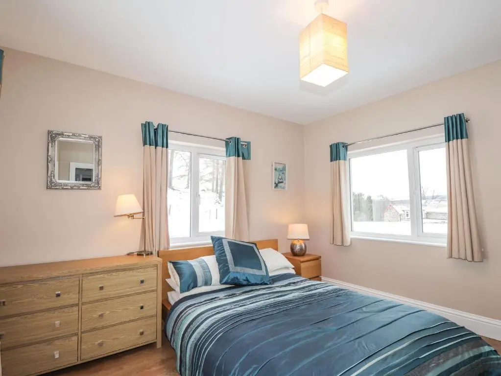 a bedroom with a bed and two windows at The Larches in Kingussie
