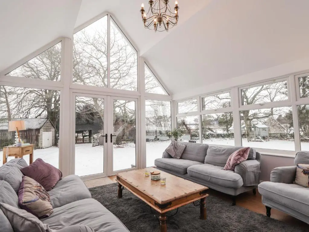 a living room with couches and a table and windows at The Larches in Kingussie