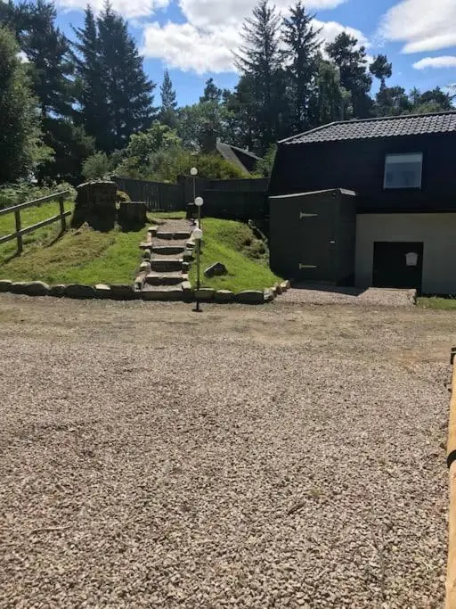 a gravel parking lot with a building and a barn at Riverside Hideaway in Kincraig