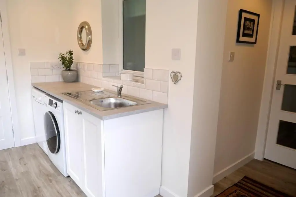 a white kitchen with a sink and a washing machine at Stewart's Cottage, Aviemore Centre in Aviemore