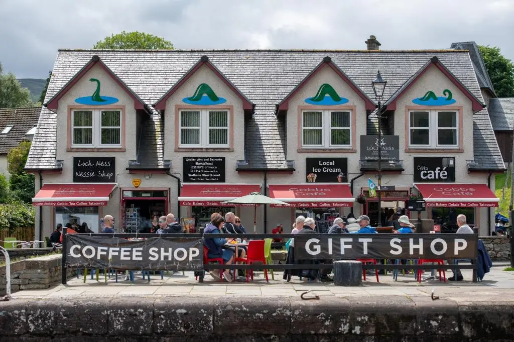 a group of people sitting at tables in front of a coffee shop at Loch Ness Gate House in Fort Augustus