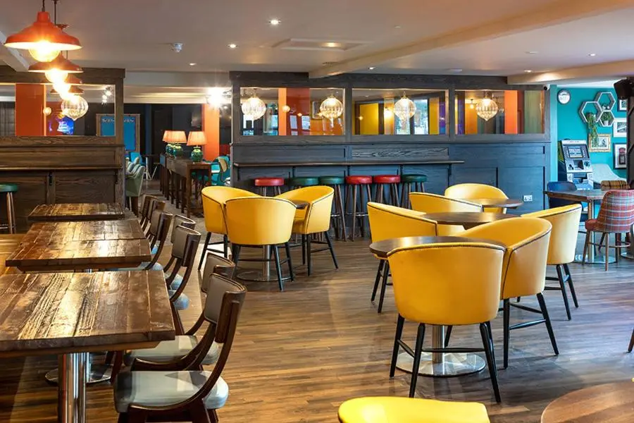 a restaurant with wooden tables and yellow chairs at Camping Pods Silver Sands Holiday Park in Lossiemouth