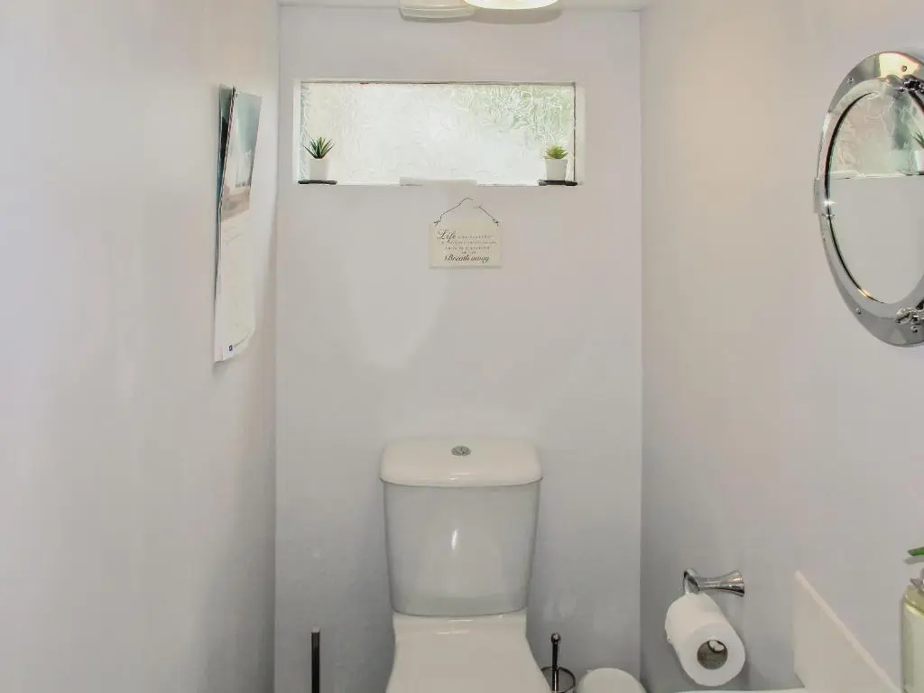 a white bathroom with a toilet and a window at Harbour Road in Gardenstown
