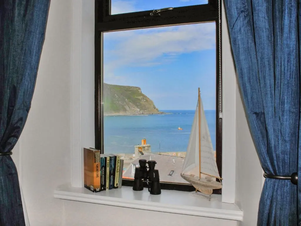 a window with a view of the ocean and a sailboat at Harbour Road in Gardenstown