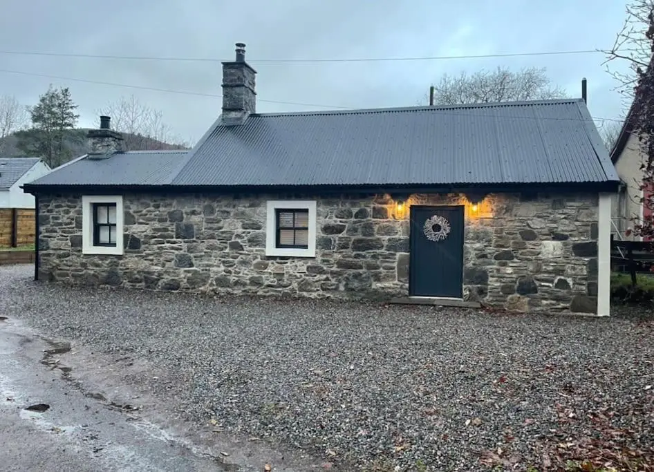 a stone house with a black door and a driveway at The Old Croft in Fort Augustus